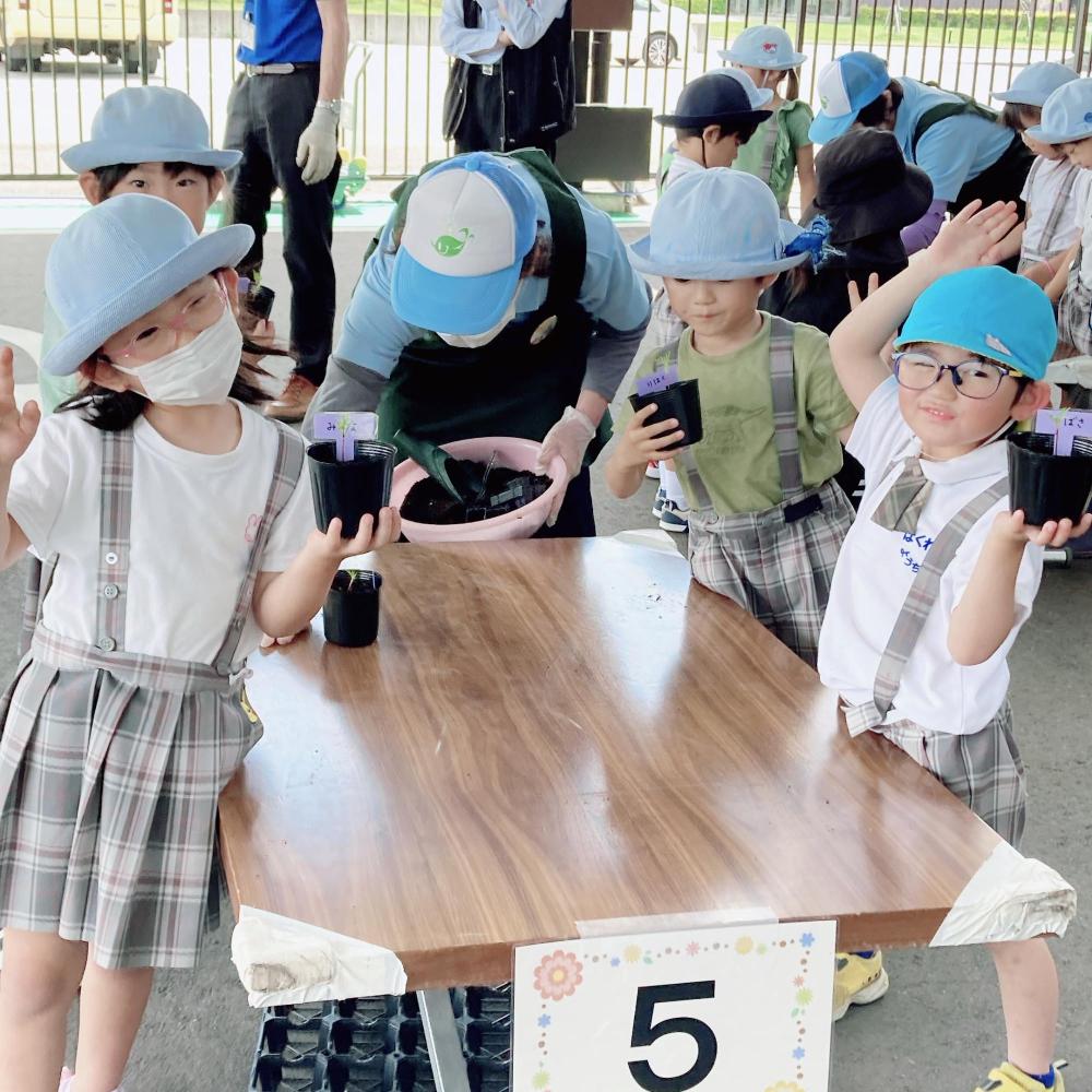 「5」の紙が貼られた机の周りで自分のポットを持ちながらおどけたポーズをとっている園児4名の写真