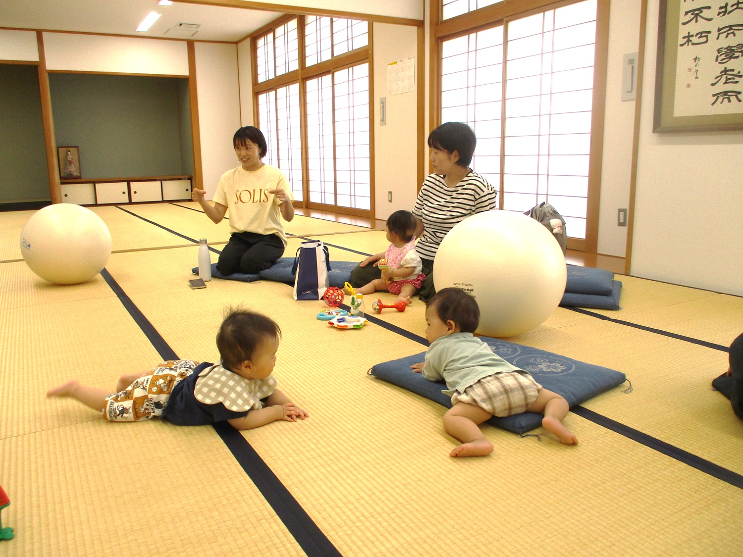 講師の説明を聞く受講生と和室のフロアーにはいはいしているベビーたち
