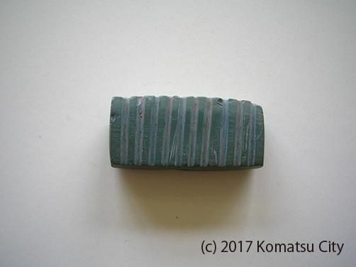 ほぼ等間隔で10本の溝が掘られた緑色の管玉の写真