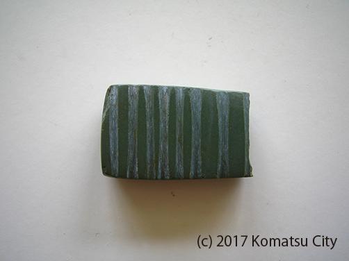 ほぼ等間隔で7本の溝が掘られた緑色の管玉の写真
