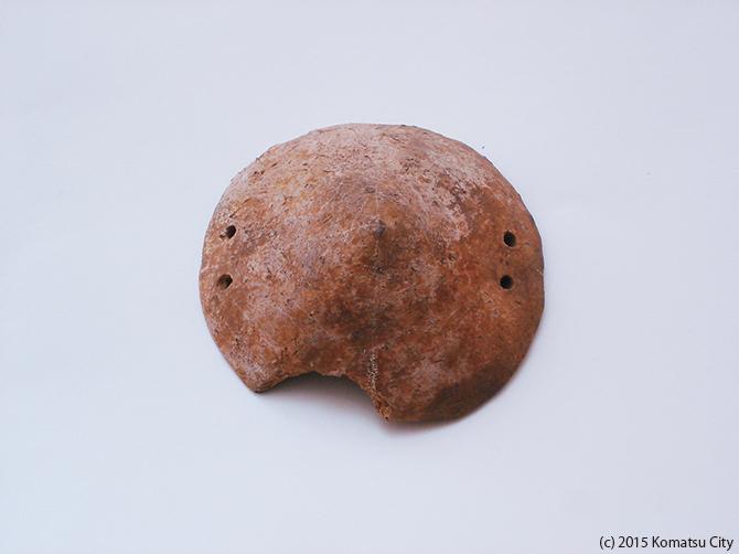 丸いとんがり帽子のような形をして全体が赤茶色、両左右に2つずつ穴があけられた蓋形土器2通番号:141の写真