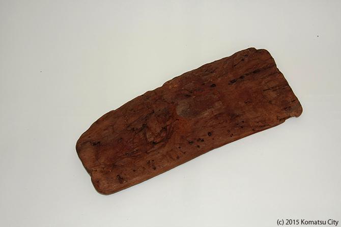 濃い茶色の長方形の平らな木の板で、片方の側面が削れて角が取れている鍬21の写真