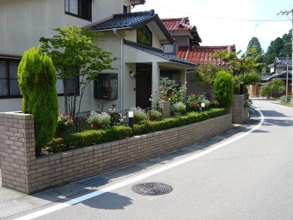 道路沿いのレンガ造りの花壇に手入れされた低木が植えてあり、柵に植木鉢が等間隔に飾られている道上邸前庭の写真
