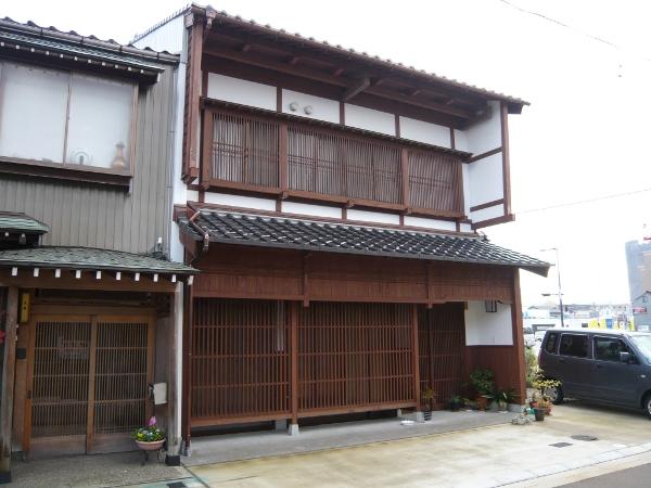 白を基調とした2階建ての四角い建物であり、窓部分には木製の茶色い格子が設置され、玄関の格子戸の前には植物が置かれている山口邸の外観写真