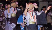 夜の道路を編み笠を被りお揃いの浴衣姿の女性たちが踊り歩いているおっしょべまつりの様子を写した写真