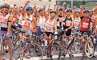 ユニフォーム姿の全日本鉄人レースの参加者の人達が自転車の横で右手を上にあげている写真