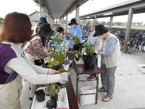 屋外で沢山の受講生と講師が机の上で寄せ植えをする様子