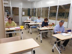 研修室の中で男女6名の参加者がモチーフを見ながら水彩画を描く様子