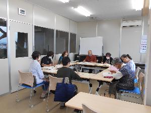 テーブルを参加者が囲み正面に男性1名と講師が座り周りに女性6名が座り語り合う様子