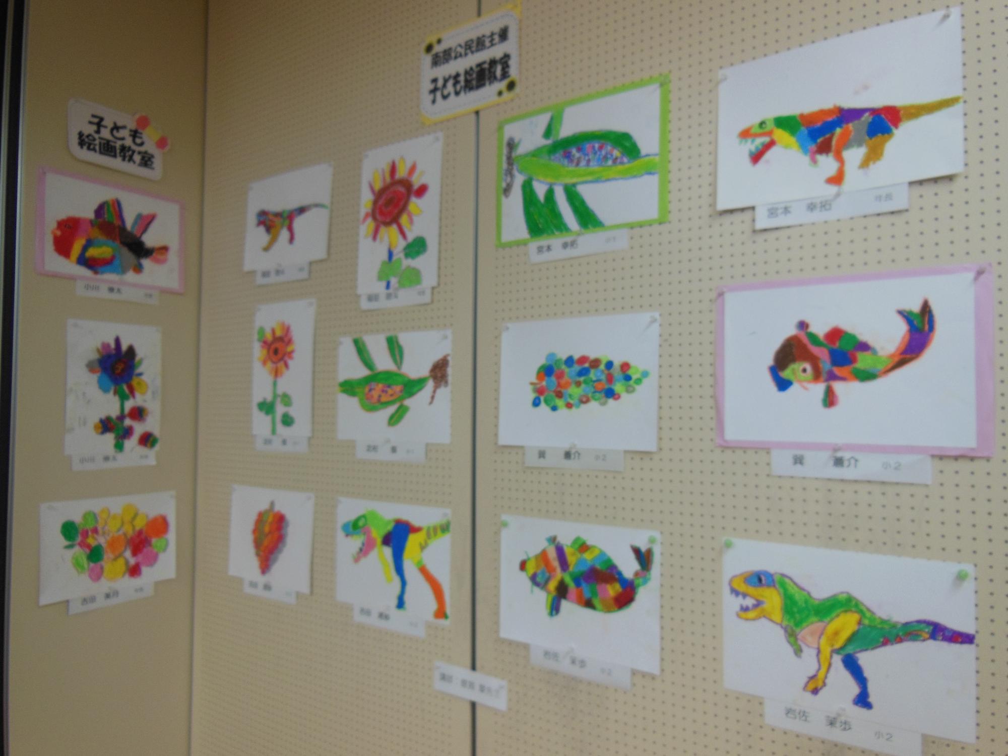 会場に生け花や絵画、机の上に色々な作品が展示されており、来場者が立ち止まって作品を見ている様子の写真