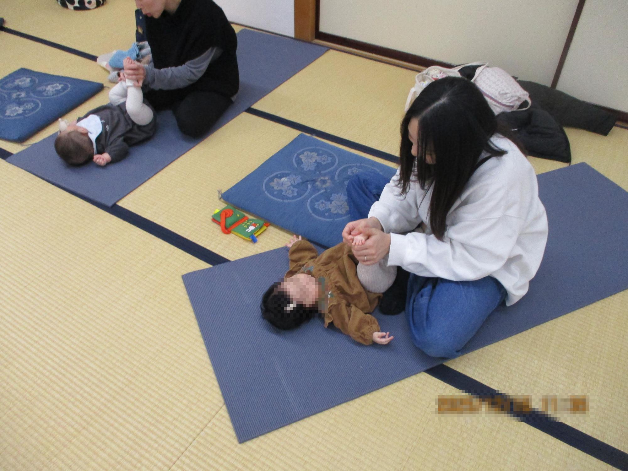 ベビーをヨガマットの上で寝ころばせて足をマッサージするママ。ママヨガの一場面