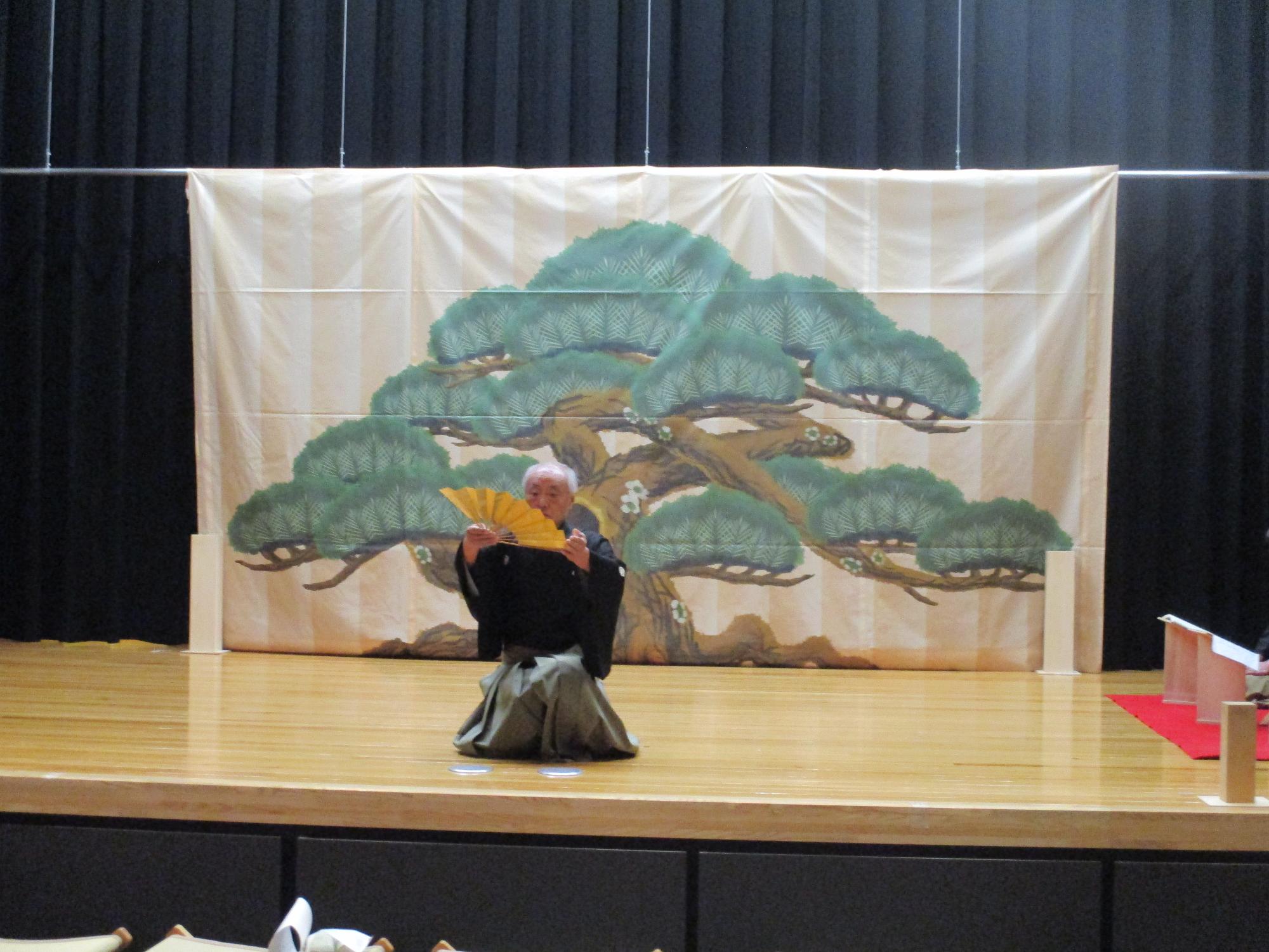 扇をもって舞台で仕舞をする男性