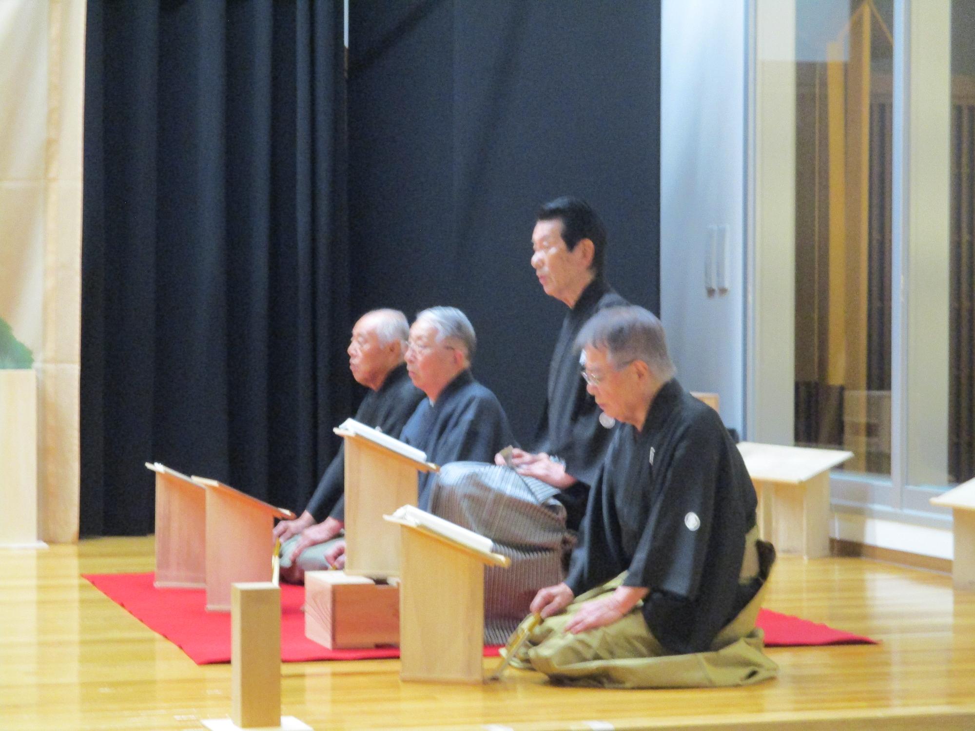 男性が4人謡をうたっている。3人は正座、一人は椅子に座って謡を行っている。