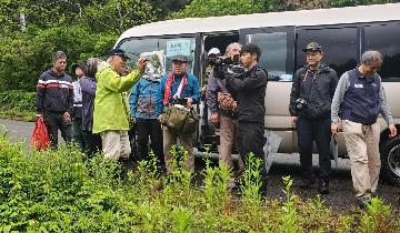 尾小屋停車場跡の前でバスを降りて説明を聞く参加者