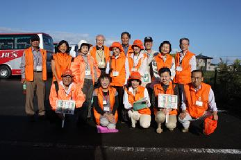 オレンジ色のベストや帽子を着用した、観光ボランティアガイドようこその皆さん15名の集合写真