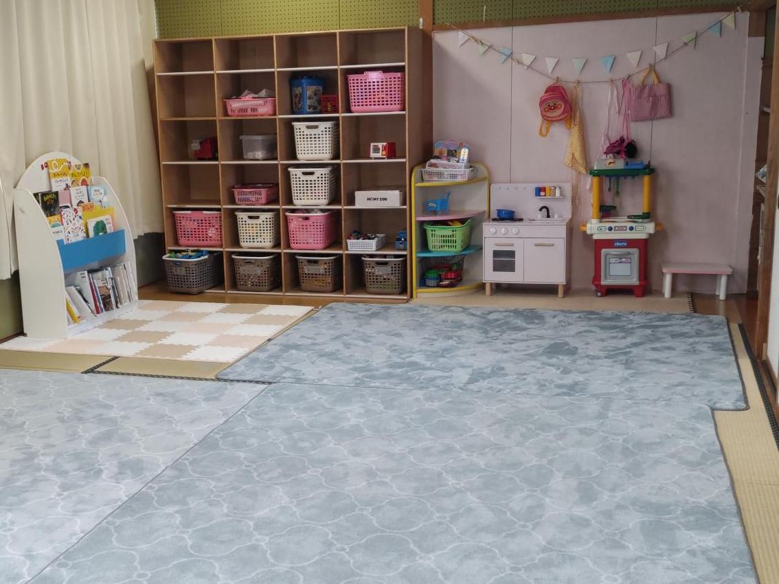 畳の部屋にやわらかいカーペットが敷いてあり、棚にはままごとやおもちゃ、絵本などがある写真